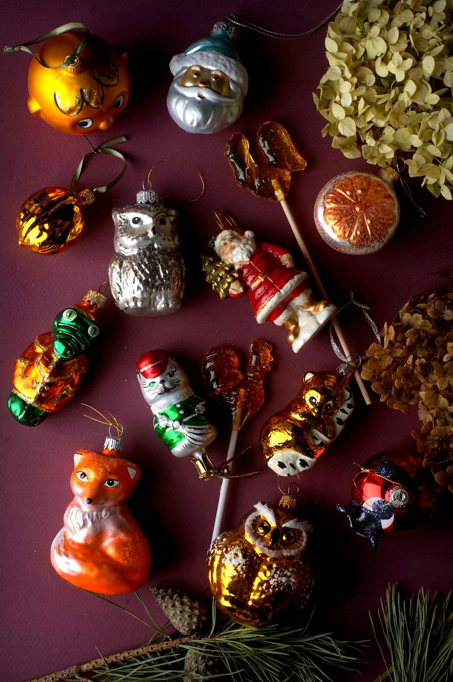 A flat lay of vintage Christmas ornaments arranged on a deep burgundy fabric background, the wine-toned palette and aged-glass texture reading as old-money traditional rather than primary-red Christmas card