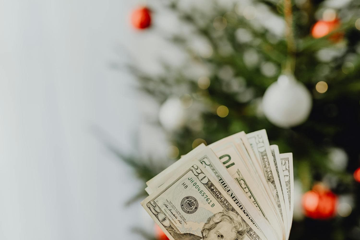 A neat stack of US dollar bills in front of a softly lit decorated Christmas tree, the kind of visual that makes the abstract idea of a Christmas decorating budget concrete