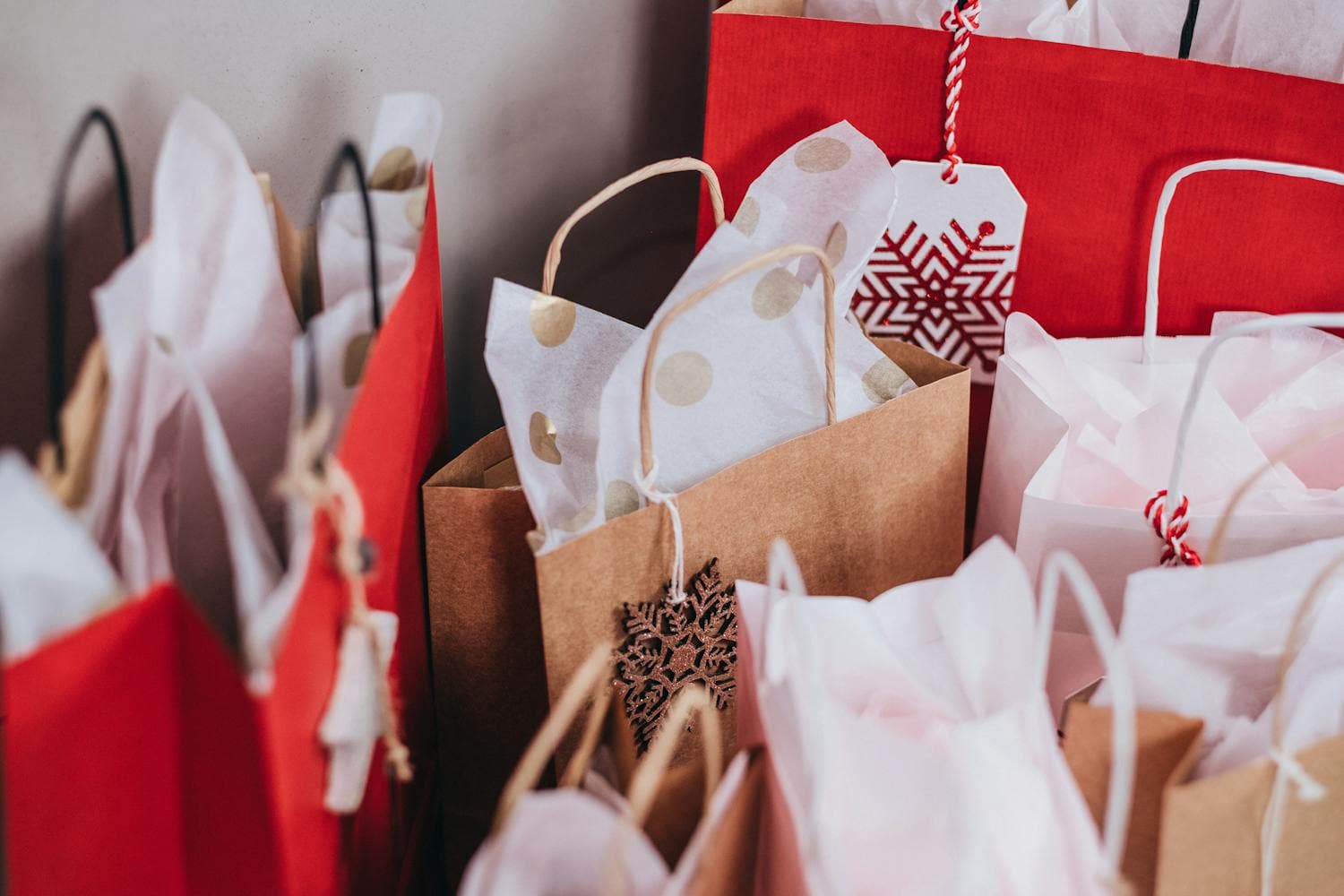 A row of festive paper shopping bags lined up against a clean white wall, the kind of haul that adds up fast when impulse purchases pile up at the end of every December shopping trip