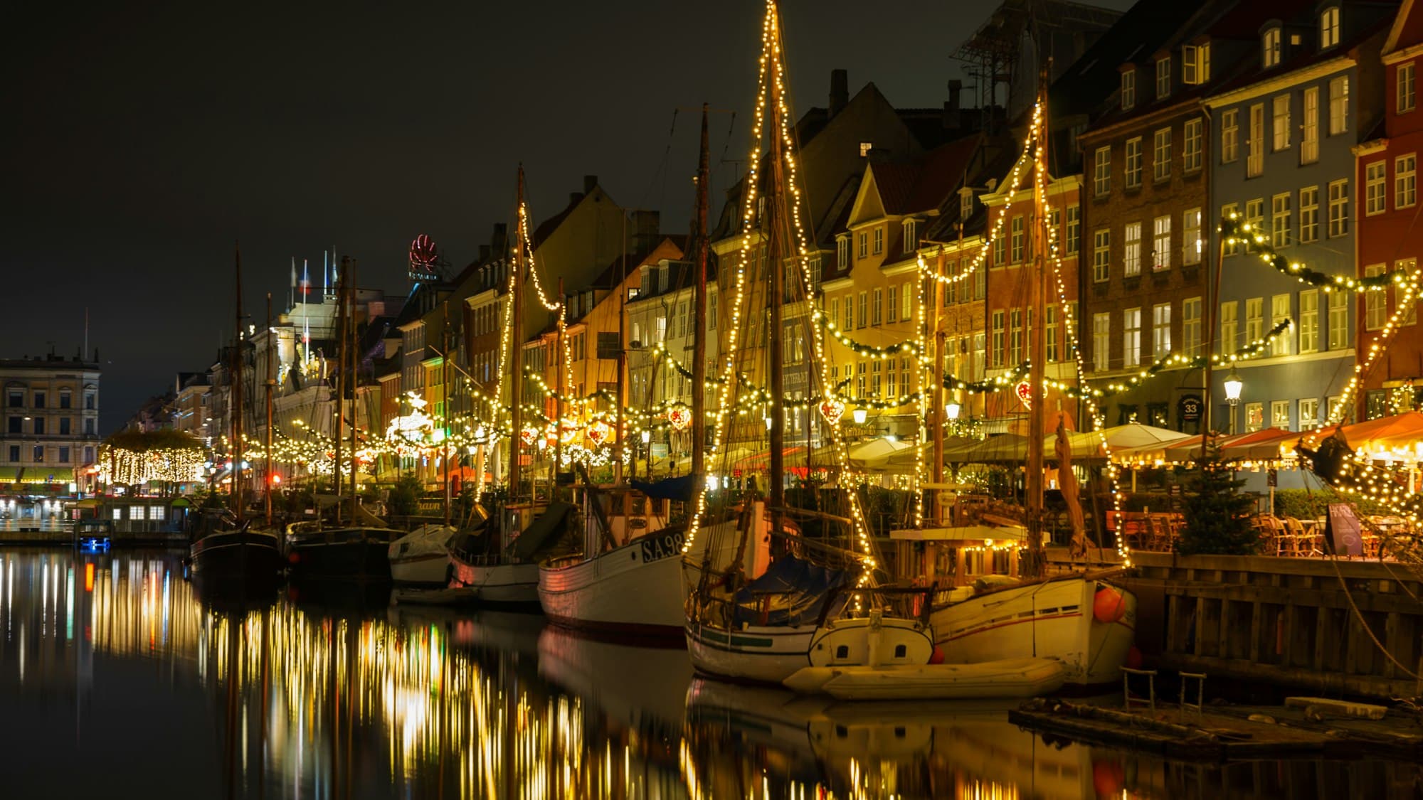 Boats and waterfront buildings reflected on a canal at night in Copenhagen, Denmark, during the Christmas season