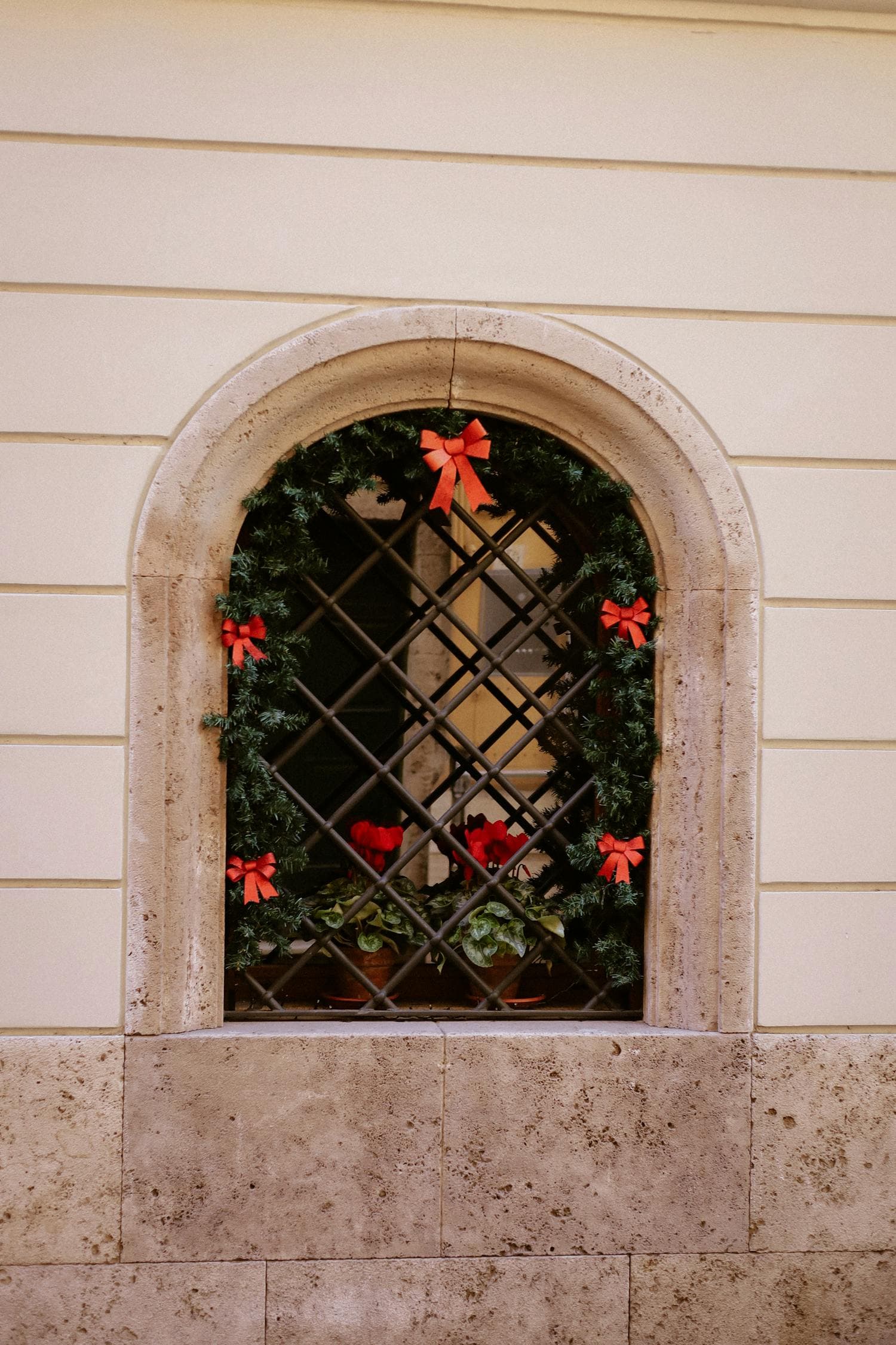 A traditional arched window framed by weathered stone, decorated with a simple fresh evergreen wreath tied with a deep red ribbon and a matching red bow, the kind of restrained Christmas moment Cape Cods reward
