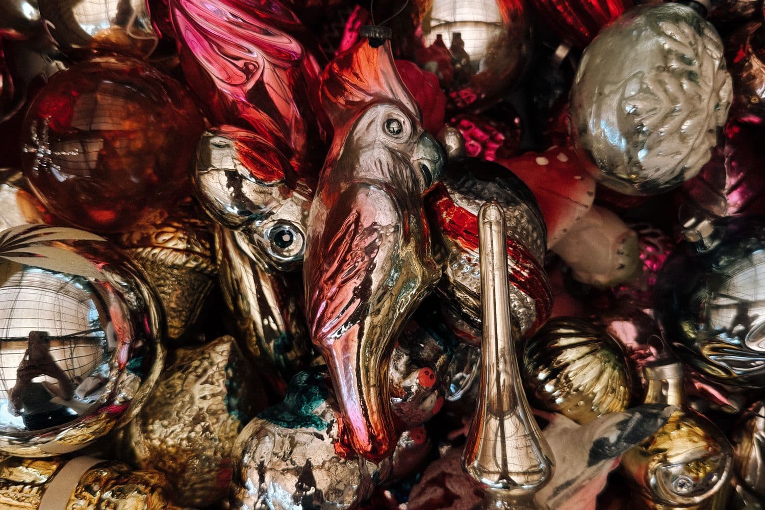 A cluster of vintage mercury-glass Christmas ornaments in rich reds, silvers, and golds, including a hand-painted bird ornament