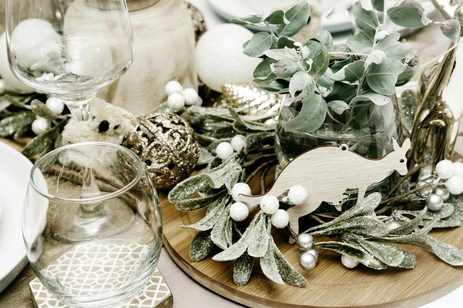 A tastefully set Christmas dining table with cream linens, glassware, eucalyptus stems and sage greenery running down the center, and matte black candlesticks, the layered-but-restrained look that defines a modern farmhouse holiday tablescape