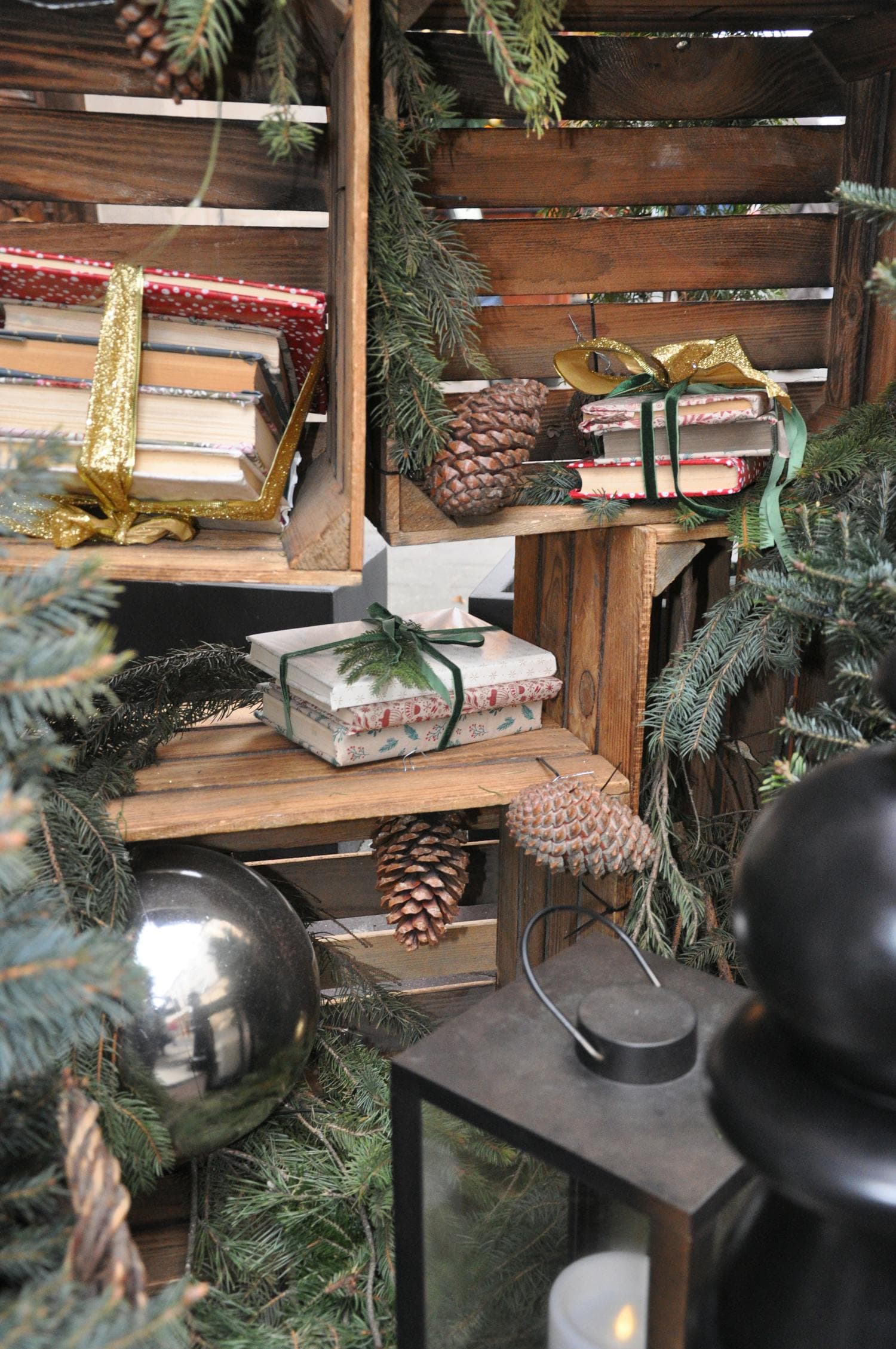 A cozy holiday composition of books wrapped in kraft paper and tied with twine, arranged on a wooden surface alongside fresh pinecones and evergreen sprigs, the visual centerpiece of the wrapped-books advent tradition