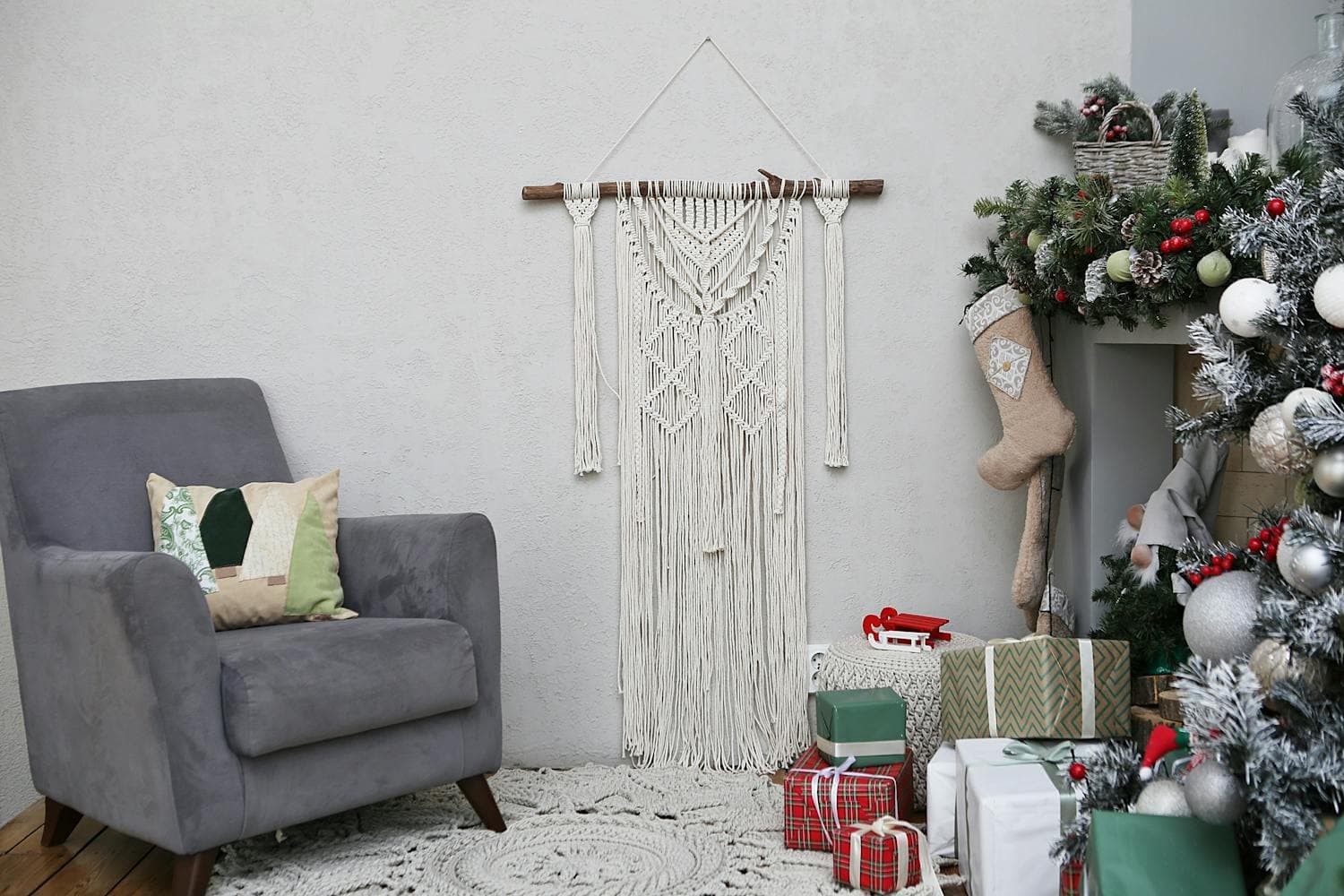 A Scandinavian-style reading nook with a soft gray upholstered armchair, a cream knit throw draped across the back, a stack of wrapped books beside the chair, and warm low lighting, the kind of jolabokaflod-ready corner the whole style is built around