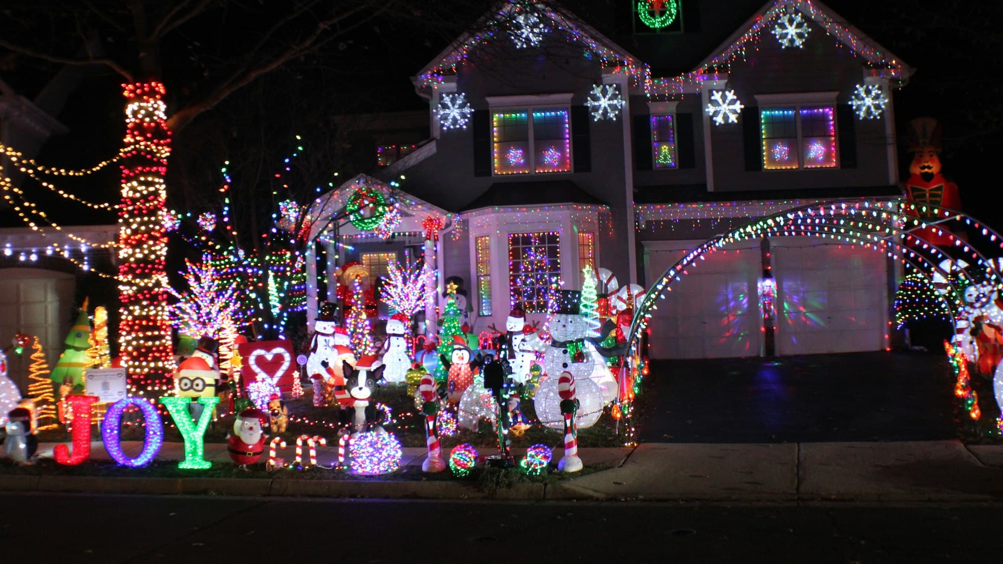 A suburban house exterior covered in warm Christmas lights and decorations, glowing at dusk