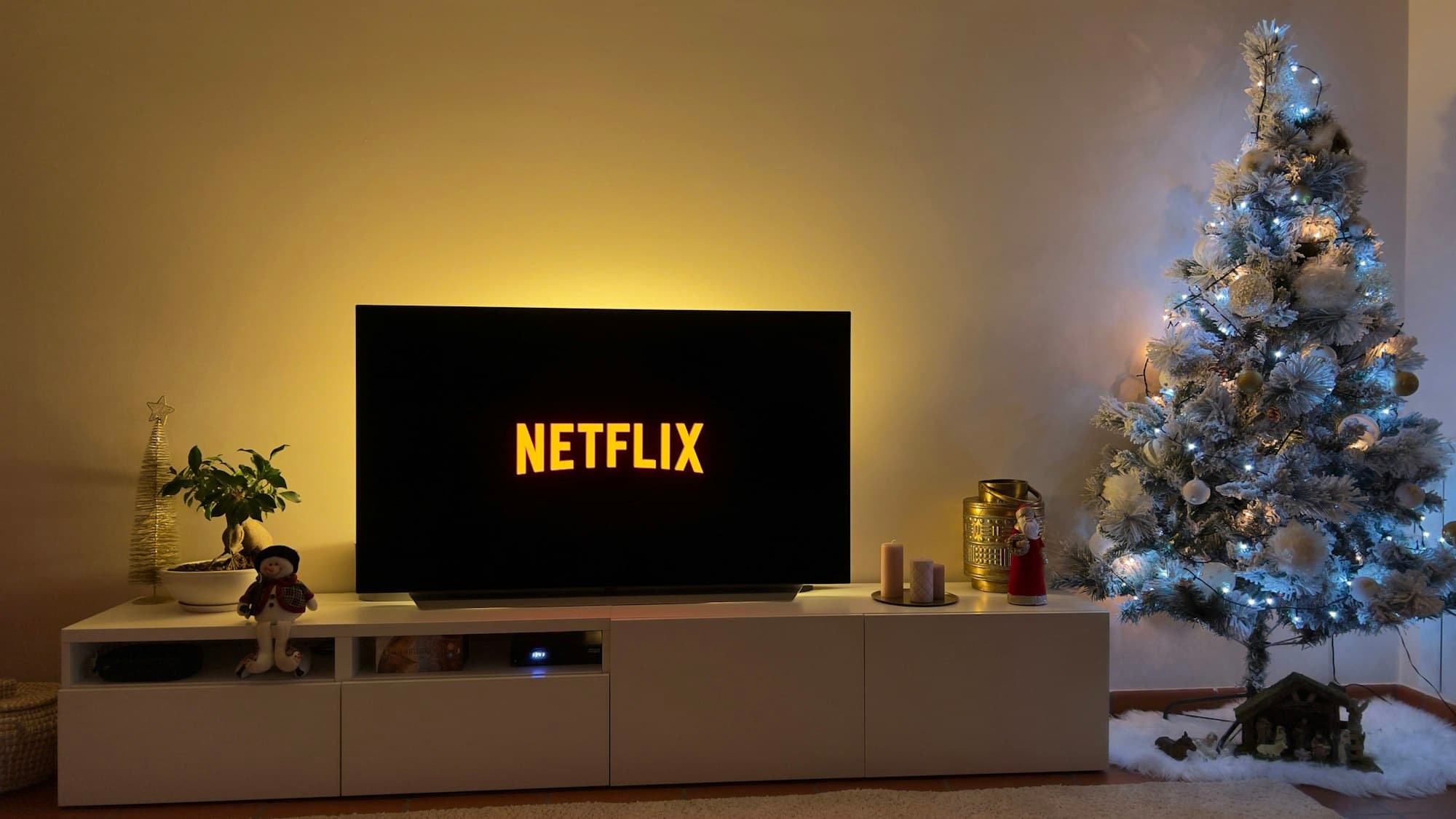A living room set up for a Christmas movie night, with a television beside a lit, frost-flocked tree