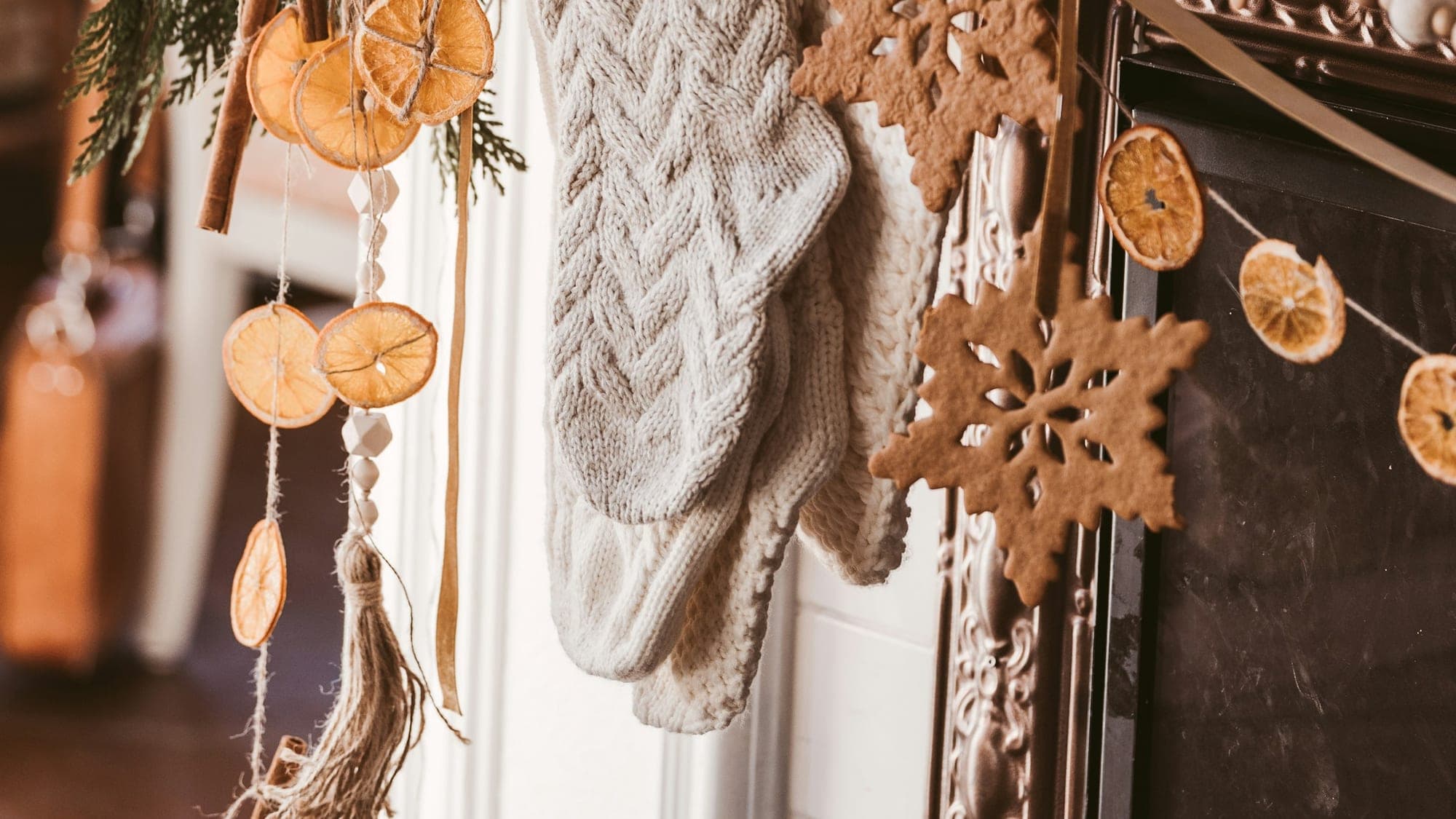 A cream cable-knit Christmas stocking on a white mantel with cedar garland, dried orange slices, cinnamon sticks, and gingerbread snowflake ornaments