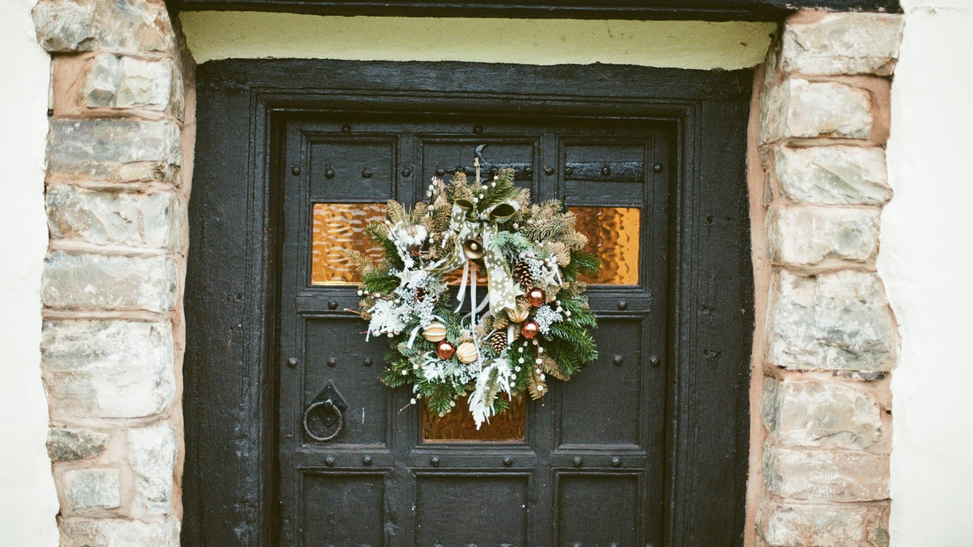 A full mixed-evergreen Christmas wreath hanging on a dark wooden front door