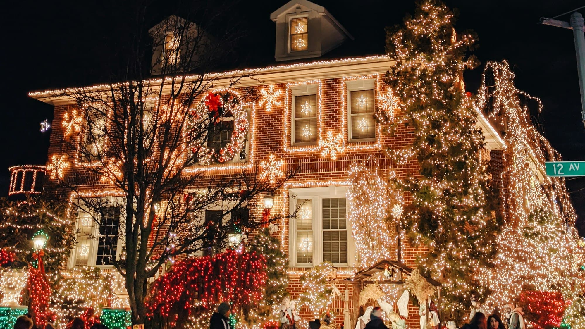 A brick house richly decorated with warm white Christmas lights, wreaths, and a lit tree at night