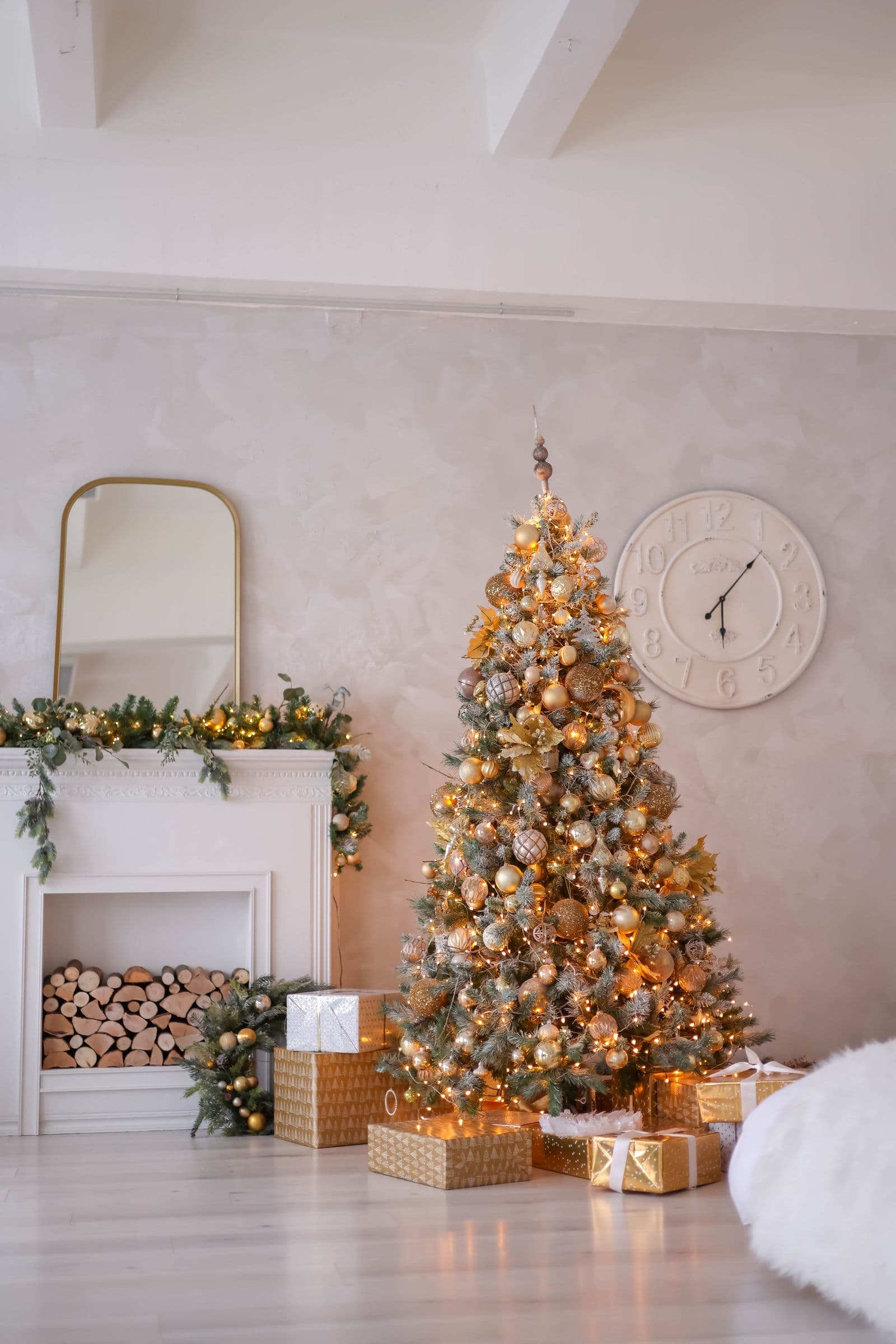An elegant living room with a gold-toned Christmas tree, a restrained lit garland on a white mantel, and coordinated wrapped gifts
