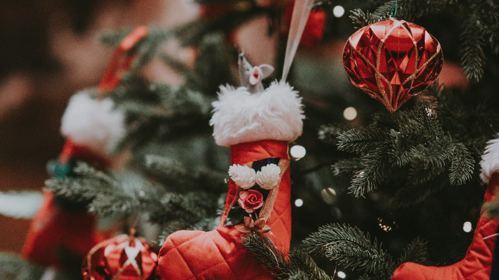 A close-up of a decorated Christmas tree with assorted ornaments layered at varying depths and sizes, lit warmly from within