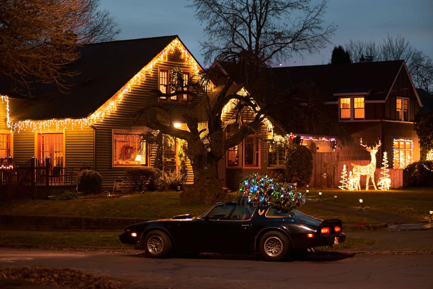 A two-story house at dusk with warm white lights outlining the roofline, eaves, and gable, glowing softly against a deep blue winter sky