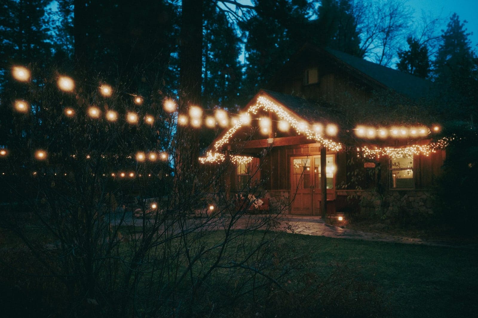 A home exterior at dusk with warm white string lights outlining the roofline and gable, and more lights strung across the yard