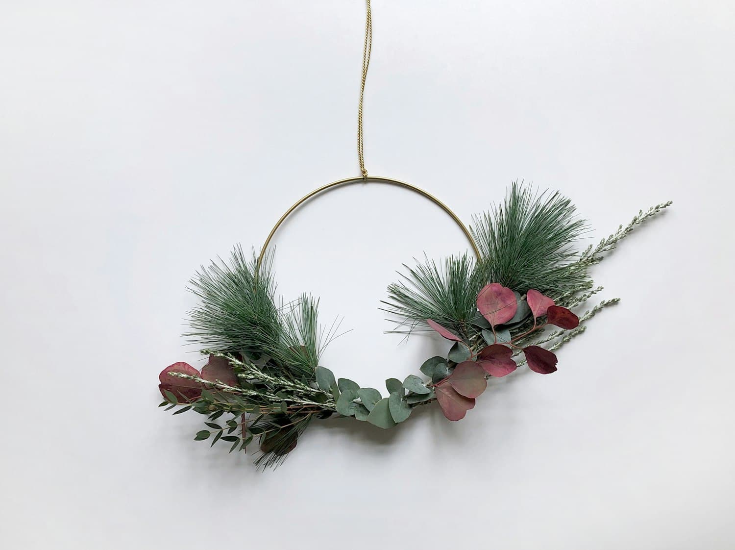 Brass hoop wreath with asymmetric eucalyptus, pine, and dried foliage on a clean white wall