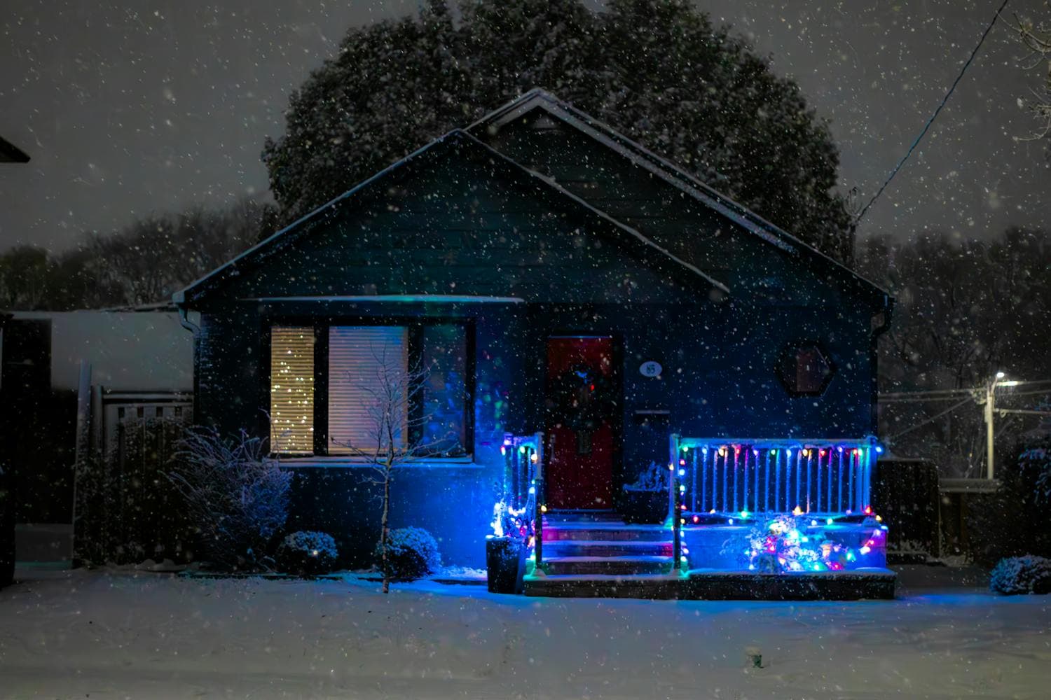 A cozy single-story home illuminated by warm Christmas lights at night with snow covering the yard, capturing the unbroken horizontal silhouette that defines the ranch architectural style