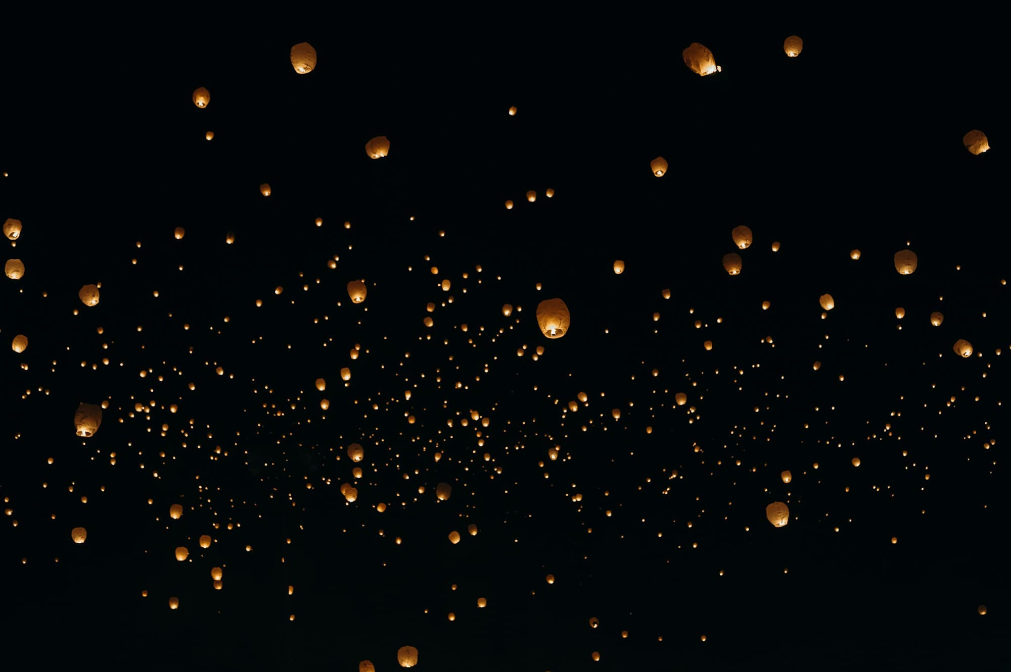 Hundreds of glowing paper sky lanterns drift upward against a pitch-black night sky, scattered at varying heights from foreground to distance, capturing the Argentine globos tradition of releasing paper hot-air lanterns at midnight on Christmas Eve