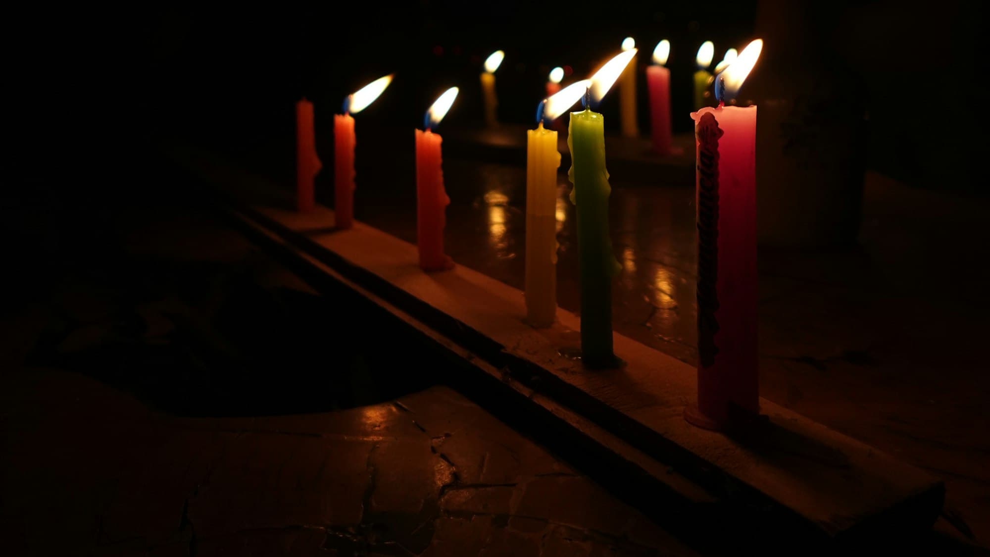 Rows of colorful lit candles glowing in the dark, the kind set out for Día de las Velitas that opens Colombia's Christmas season